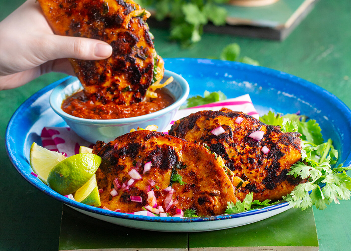 Tre birria tacos på et fat hvor den ene dyppes i saus