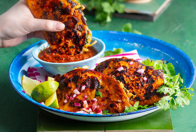 Tre birria tacos på et fat hvor den ene dyppes i saus